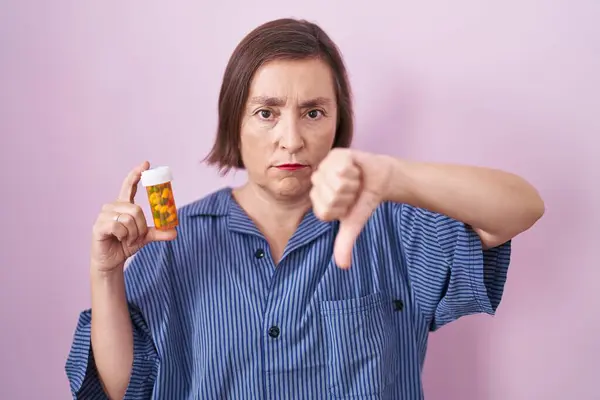 怒った顔の丸薬を持っている中年のパニック女性 親指で嫌いを示す負の兆候ダウン 拒絶概念 — ストック写真