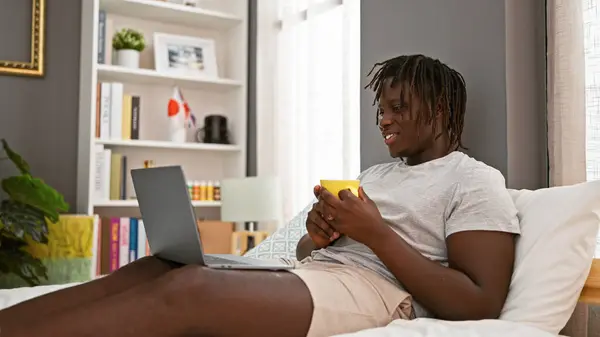 African american man doing video call drinking coffee at bedroom