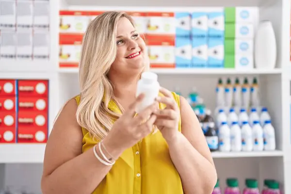 Young woman customer smiling confident holding pills bottle at pharmacy