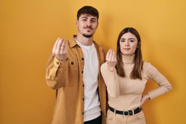 Sarı arka planda duran genç İspanyol çift ellerinde ve parmaklarında kendinden emin ifadeyle italyan jestleri yapıyor. 