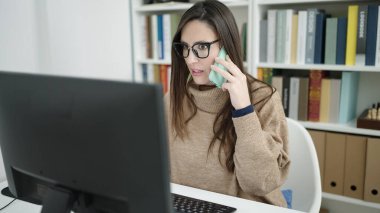 Güzel İspanyol kız öğrenci kütüphanede bilgisayar kullanıyor. Akıllı telefondan konuşuyor.