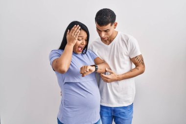 Latin kökenli genç bir çift, arka planda bir bebek bekliyor. Saate bakıyor, endişeli, geç kalmaktan korkuyor. 