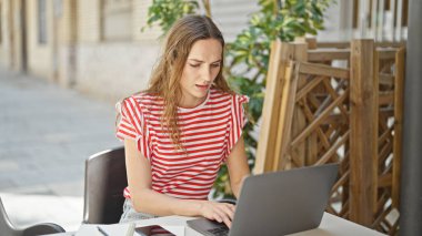 Kahve dükkanının terasında dizüstü bilgisayar kullanan genç sarışın kadın.