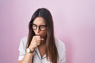Pembe arka planda duran gözlüklü genç esmer kadın kendini iyi hissetmiyor ve soğuk algınlığı veya bronşitin belirtisi olarak öksürüyor. sağlık hizmeti kavramı. 