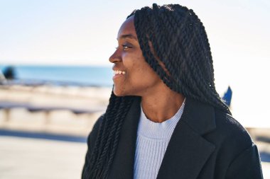 Afro-Amerikalı kadın, gülümsüyor. Kendine güveniyor, deniz kenarına bakıyor.