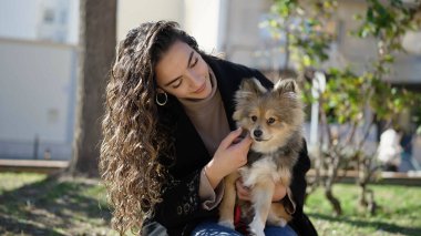 Köpeğiyle gülümseyen genç İspanyol kadın parkta bankta oturuyor.