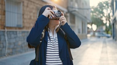 Sırt çantalı genç İspanyol kadın turist sokakta kamerayla fotoğraf çekiyor.