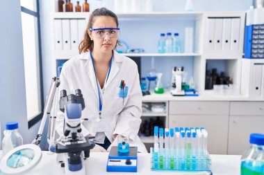 Young hispanic woman working at scientist laboratory skeptic and nervous, frowning upset because of problem. negative person. 