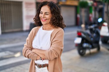 Middle age hispanic woman smiling happy with crossed arms outdoors