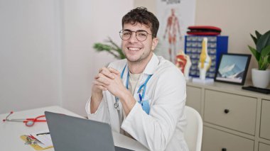 Young hispanic man doctor using laptop working at clinic