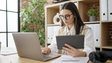 Young beautiful hispanic woman business worker using touchpad and laptop at office