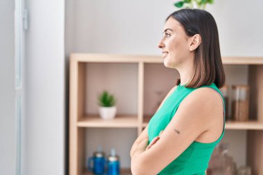 Genç İspanyol kadın gülümsüyor. Kollarını kavuşturup evde duruyor.