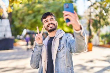 Genç İspanyol adam gülümsüyor. Parktaki akıllı telefonun yanında özçekim yapıyor.