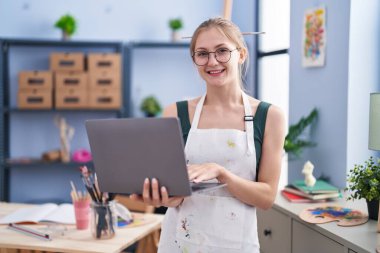 Young caucasian woman artist smiling confident using laptop at art studio