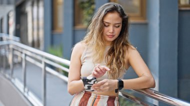 Genç, güzel, İspanyol bir kadın akıllı telefon kullanıp sokağı gözetliyor.