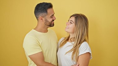 Erkek ve kadın çift gülümsüyor. Birbirlerine sarılıyorlar ve izole edilmiş sarı arka planda birbirlerine bakıyorlar.