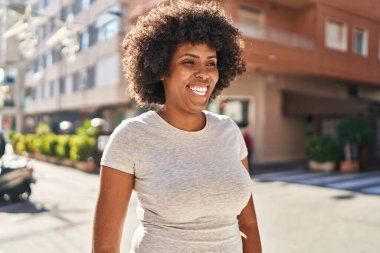 Afro-Amerikalı kadın gülümsüyor. Kendinden emin bir şekilde caddeye bakıyor.