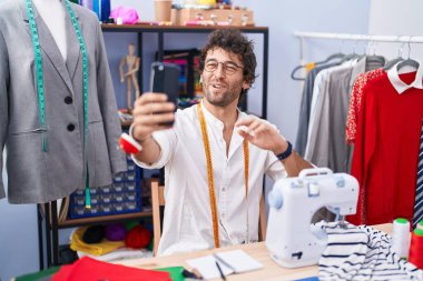 Young hispanic man tailor smiling confident having video call at clothing factory