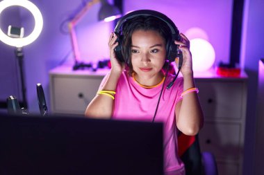 Young hispanic woman streamer smiling confident sitting on table at gaming room