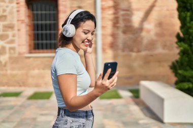 Genç İspanyol kadın sokakta müzik dinlerken kendinden emin gülümsüyor.