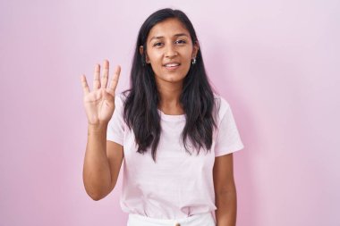 Pembe arka planda duran genç İspanyol kadın dört numarayı gösterip işaret ederken kendinden emin ve mutlu bir şekilde gülümsüyor.. 