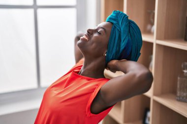 Young african american woman relaxed with hands on head sitting on chair at home