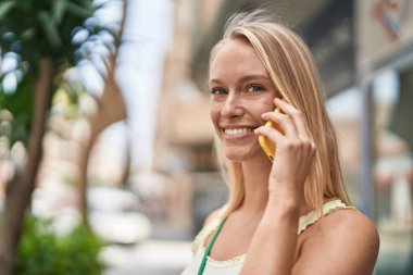 Genç sarışın kadın gülümsüyor. Kendine güveni tam. Akıllı telefondan konuşuyor.