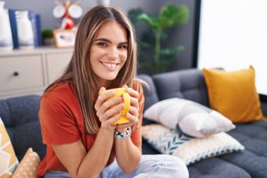 Genç ve güzel İspanyol kadın evdeki kanepede oturup kahve içiyor.