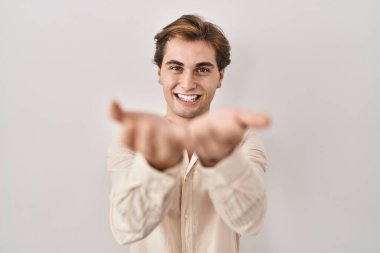 Young man standing over isolated background smiling with hands palms together receiving or giving gesture. hold and protection 