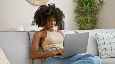 African american woman using laptop sitting on sofa at home
