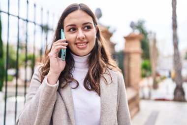Genç, güzel, İspanyol bir kadın gülümsüyor ve caddede akıllı telefondan konuşuyor.