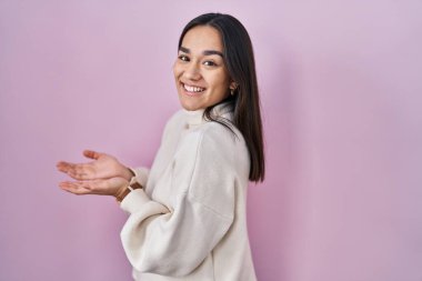 Pembe arka planda duran genç Güney Asyalı kadın avuçlarını açıp fotokopi alanını gösteriyor, gülümseyerek mutlu bir gülümseme sunuyor. 