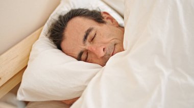 Orta yaşlı bir adam yatakta uzanıyor, yatak odasında uyuyor.