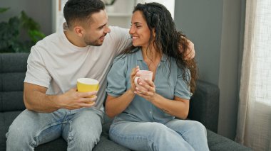 Man and woman couple sitting on sofa drinking coffee at home
