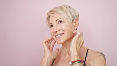 Orta yaşlı, sarışın, kendine güvenen, pembe arka planda, kendine güvenen bir kadın.