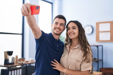 Genç İspanyol iş adamları ofiste akıllı telefonla selfie çekiyorlar.