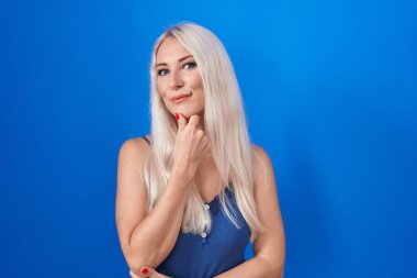 Mavi arka planda duran beyaz kadın kameraya kollarını kavuşturup gülümseyen ve çenesini kaldıran kendinden emin bir şekilde bakıyor. Olumlu düşünmek. 