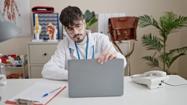 Young hispanic man doctor using laptop working at clinic