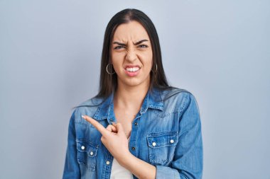 Mavi arka planda dikilen İspanyol kadın endişeli ve endişeli bir ifade takınıyor. 