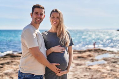 Erkek ve kadın bir arada, deniz kenarında göbeğe dokunuyorlar.
