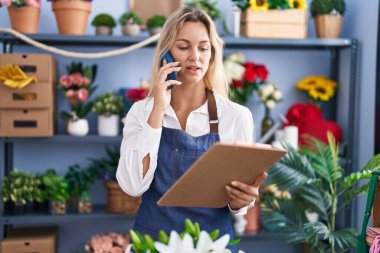 Genç sarışın kadın çiçekçi çiçekçide akıllı telefondan kitap okuyor.