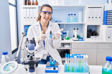 Laboratuvarda çalışan genç İspanyol kadın mutlu ve komik yüzüyle kamerayı işaret ediyor. iyi enerji ve titreşimler. 