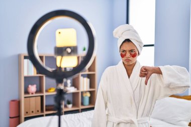 Koyu renk saçlı İspanyol bir kadın akıllı telefonlu güzellik dersleri kaydediyor. Kızgın yüzlü, negatif işaretli, baş parmakları aşağıda, reddedilme kavramından hoşlanmadığını gösteriyor. 