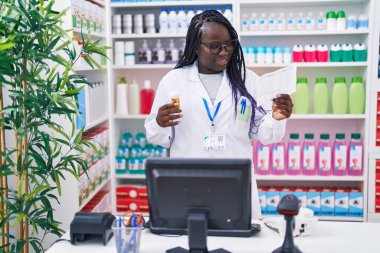 Afrika kökenli Amerikalı kadın eczacı elinde ilaç şişesiyle eczanede reçete okuyor.