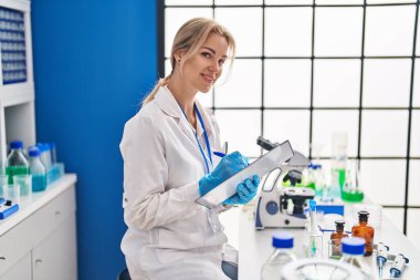 Genç sarışın bilim adamı. Laboratuvarda belgeye yazı yazıyor.