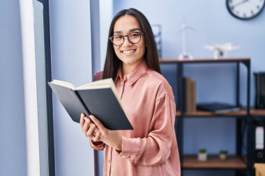 Genç İspanyol iş kadını ofiste kitap okuyor.