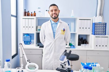 Young latin man scientist smiling confident standing at laboratory