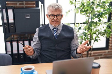 Orta yaşlı, kır saçlı iş adamı ofiste video görüşmesi yapıyor.