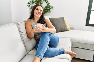 Genç ve güzel İspanyol kadın evdeki kanepede oturup kahve içiyor.