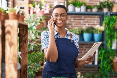 Afrikalı Amerikalı kadın çiçekçi çiçekçide akıllı telefondan not defteri okuyor.